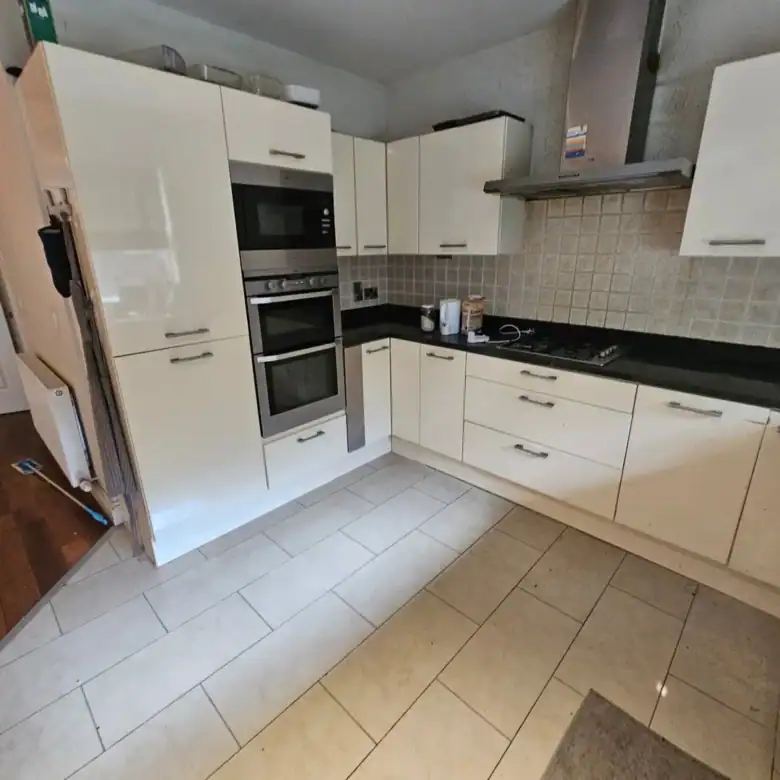 Modern kitchen with cream cabinets, black countertops, and tile flooring.