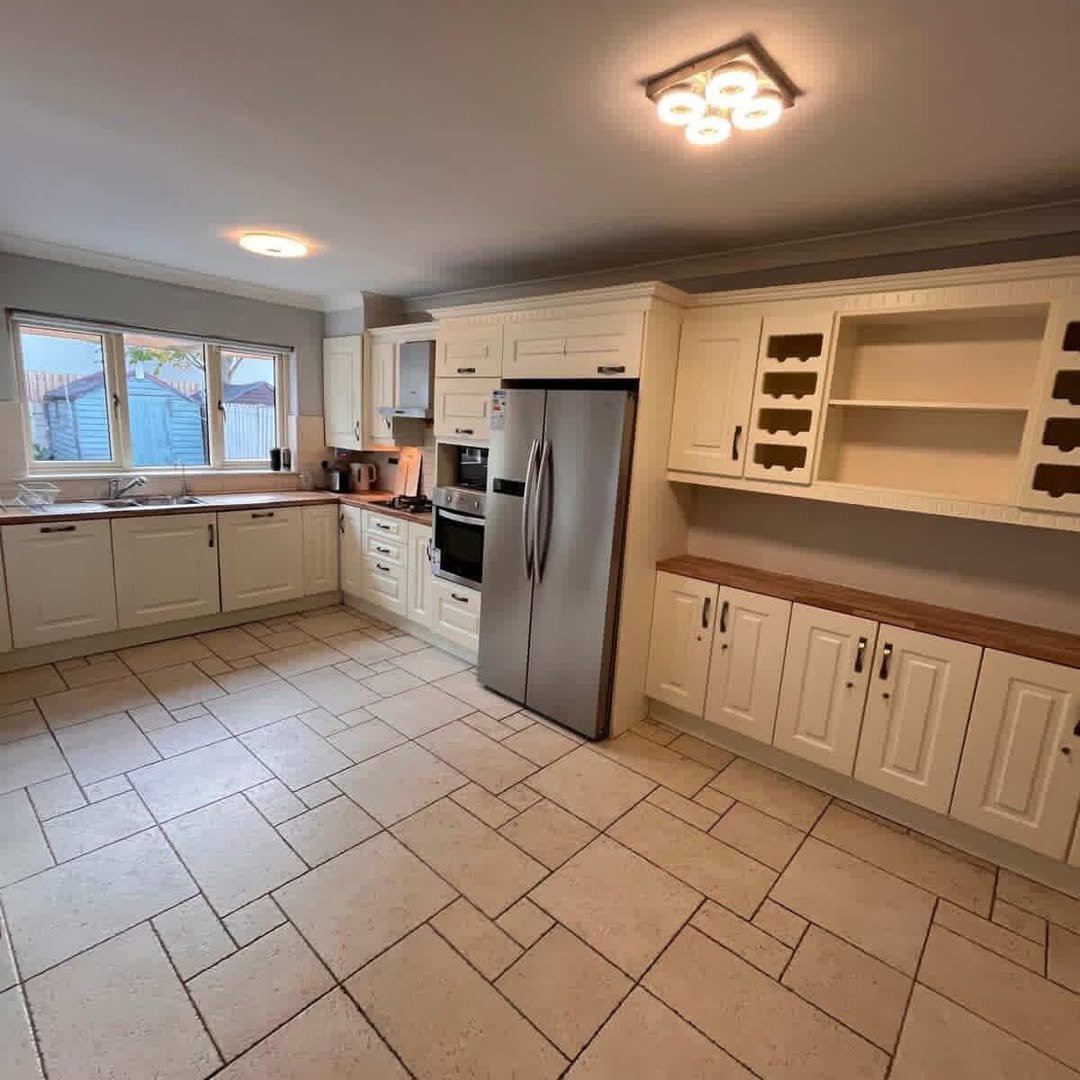 Spacious kitchen with cream cabinets, stainless steel refrigerator, tile floor, and natural light from a window.
