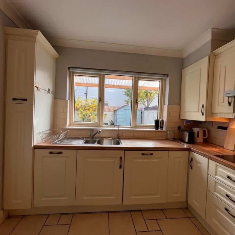 Cream kitchen with window overlooking garden, sink, and cabinets.