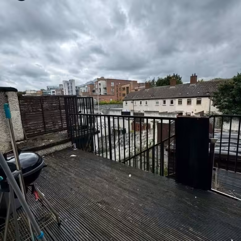 Overcast view from a deck with a grill, showing urban buildings and fences in the background.