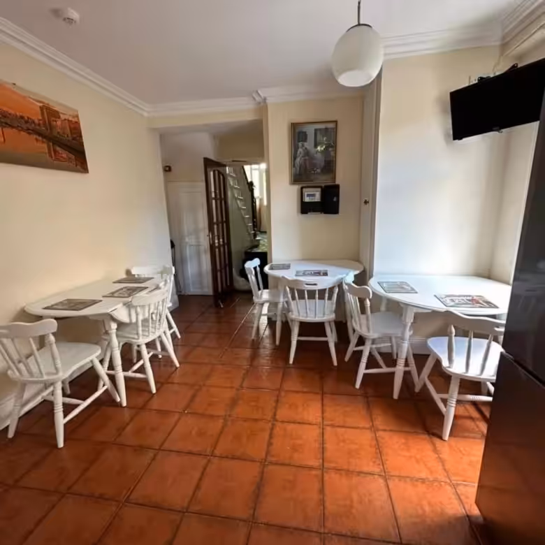 Cozy dining area with white tables, chairs, and terracotta tile flooring.