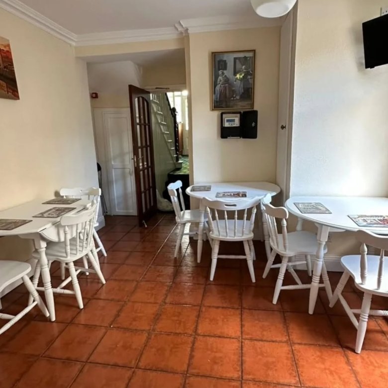 Cozy dining room with white tables, chairs, and terracotta tile flooring leading to a hallway and stairs.