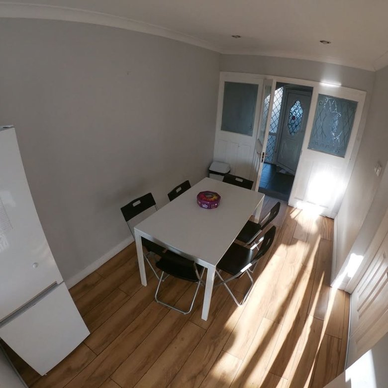 Dining area with white table, black chairs, fridge, and natural light from doors.