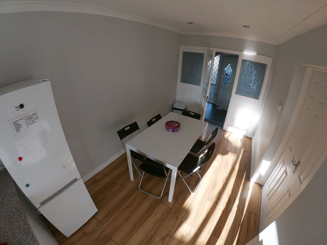 Dining area with white table, black chairs, fridge, and natural light from doors.
