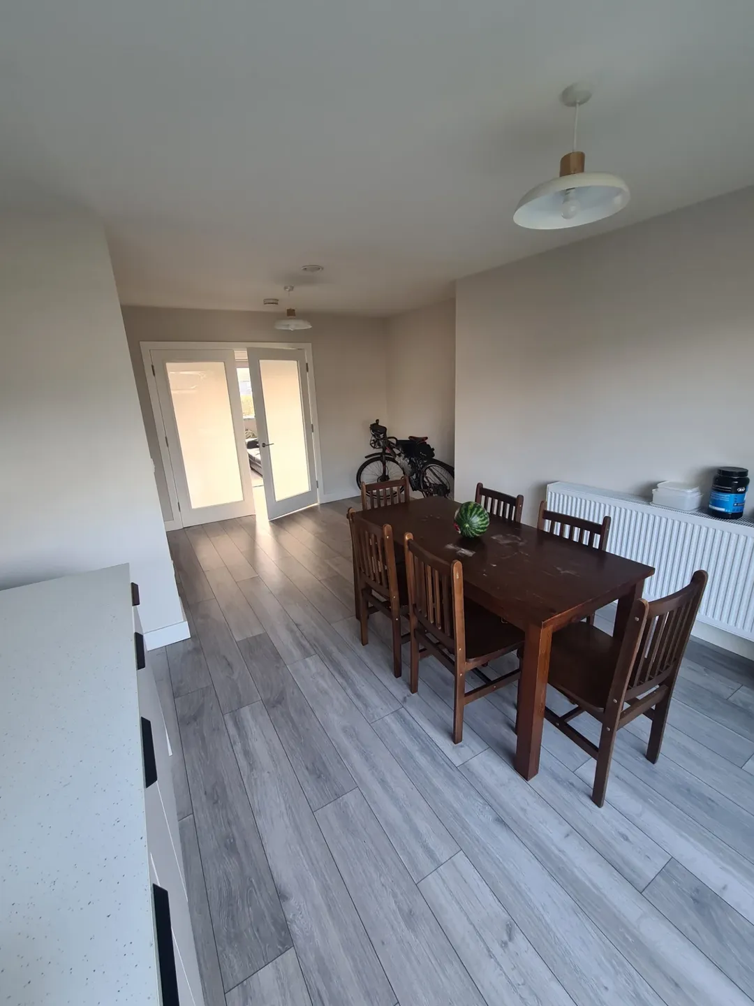 Dining room with wooden table and chairs, grey wood floors, and frosted glass doors.