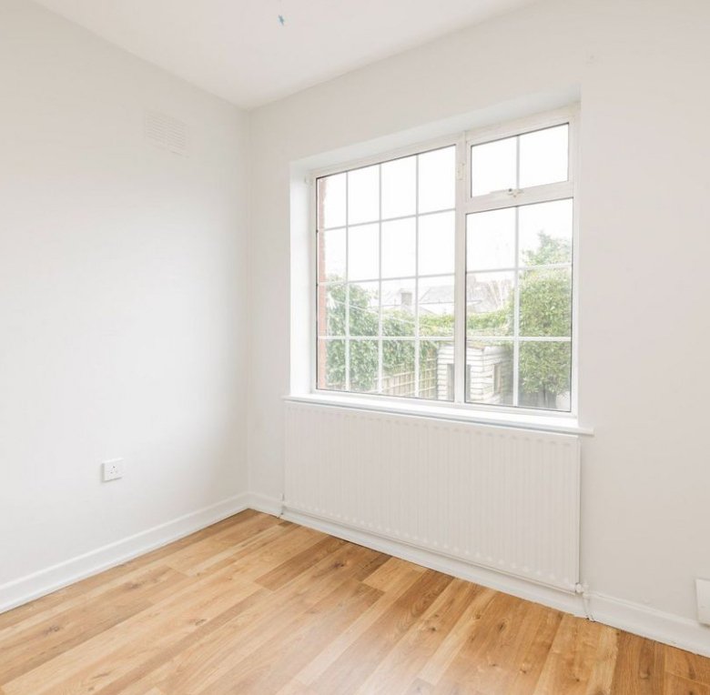 Bright, empty room with wood floor, white walls, window view of garden.