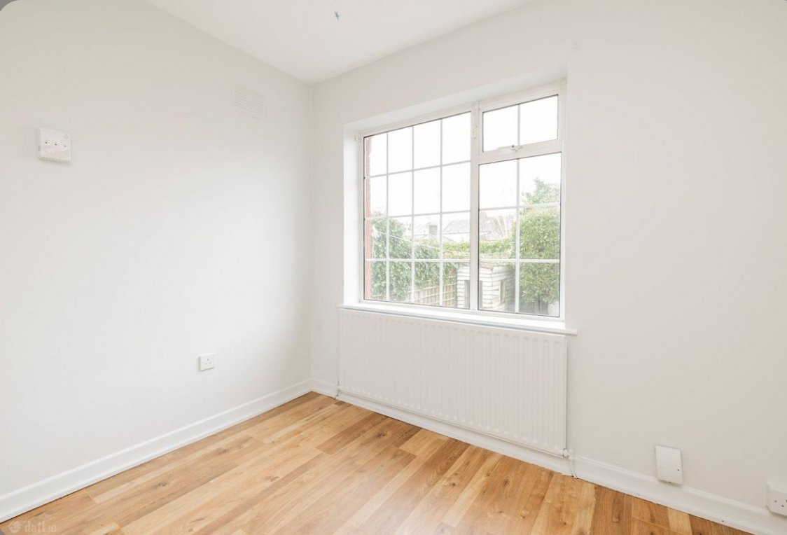 Bright, empty room with wood floor, white walls, window view of garden.