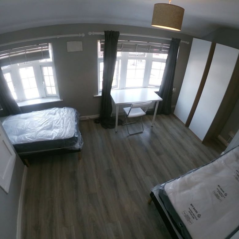 Bright room with two beds, desk, and wardrobes under large windows.