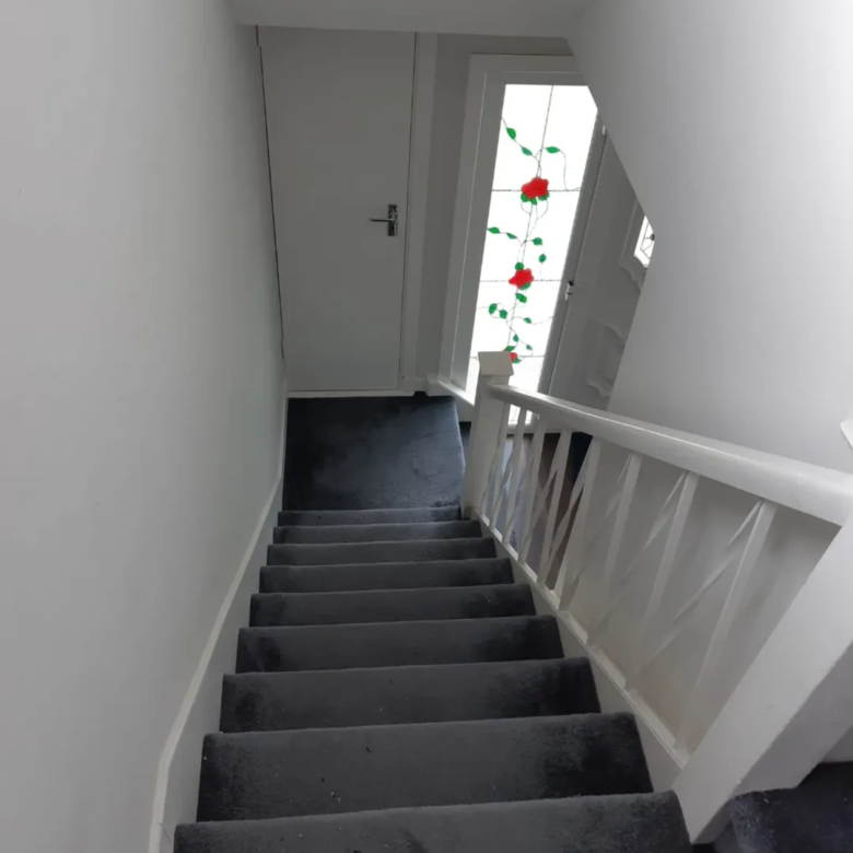 Stairway with gray carpet and white banister leads to a door with rose stained glass.