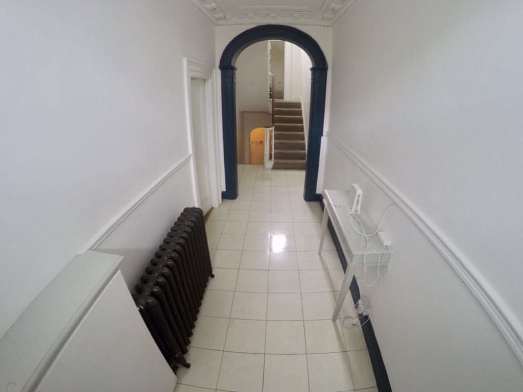 Hallway with radiator, table, and archway leading to stairs. White walls and tiled floor.