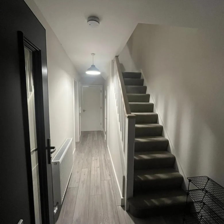 Hallway with stairs and gray wood-look flooring, white walls, and black door.