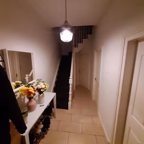 Hallway with stairs, mirror, flowers, and shoe rack under a pendant light.
