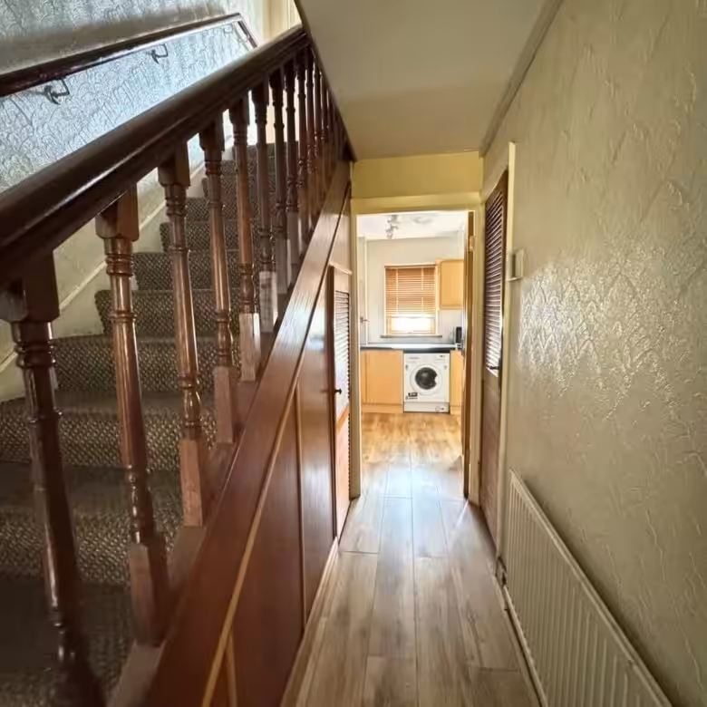 Hallway view with stairs, wood flooring, and glimpse into kitchen.