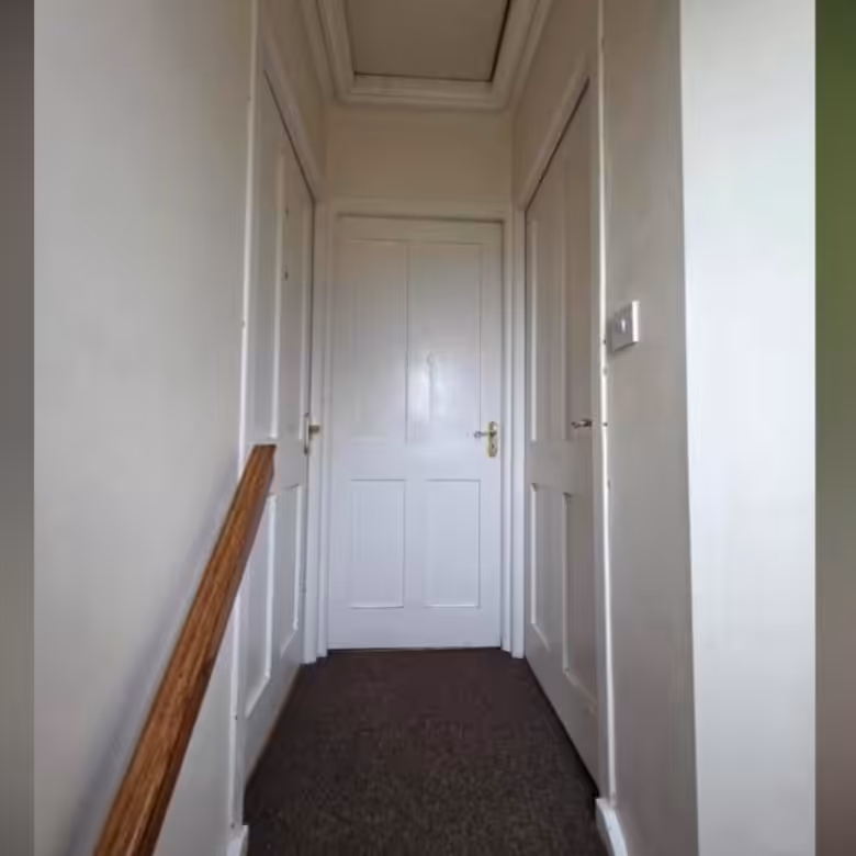 Hallway with white doors and dark carpet, leading to an attic hatch.