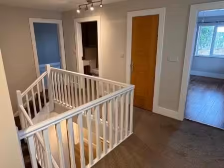 Hallway with white railing, wooden door, and doorways to other rooms.