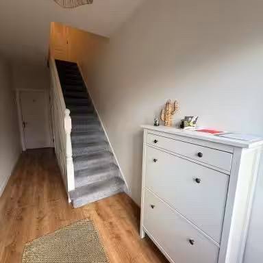 Hallway with white shoe cabinet, stairs, and wood flooring.