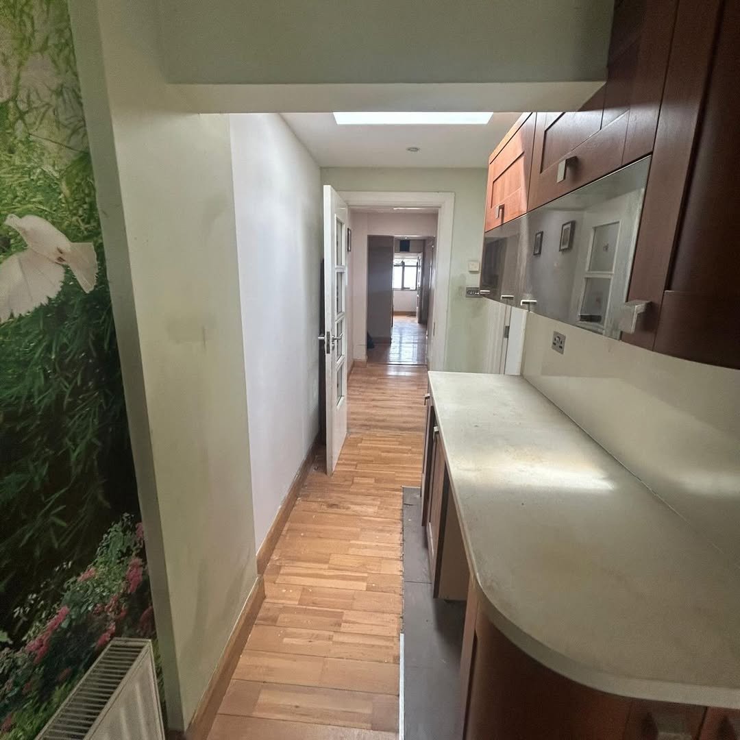 Hallway with wood floors, doors, and kitchen cabinets. Skylight provides natural light.