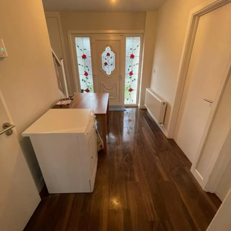 Hallway with dark wood floors, white walls, rose-decorated door, and white cabinet.