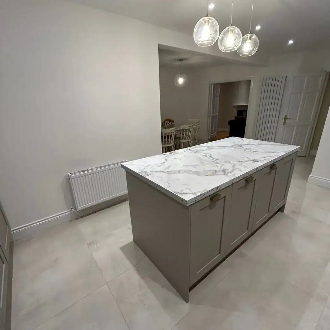 Kitchen island with marble countertop and gray cabinets under pendant lights.
