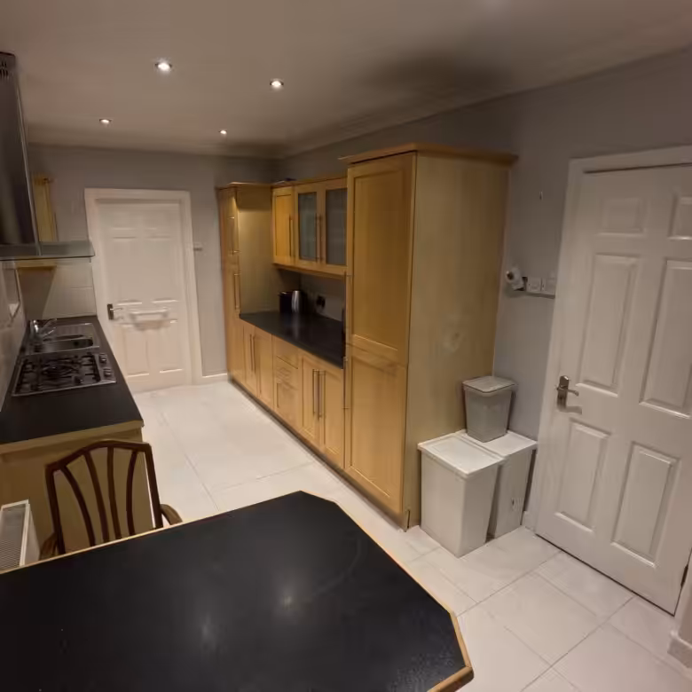 Kitchen with light wood cabinets, black countertops, and white tiled floor.