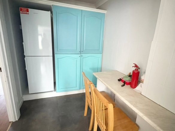 Kitchen nook with blue cabinets, white fridge, counter, and wooden chairs.