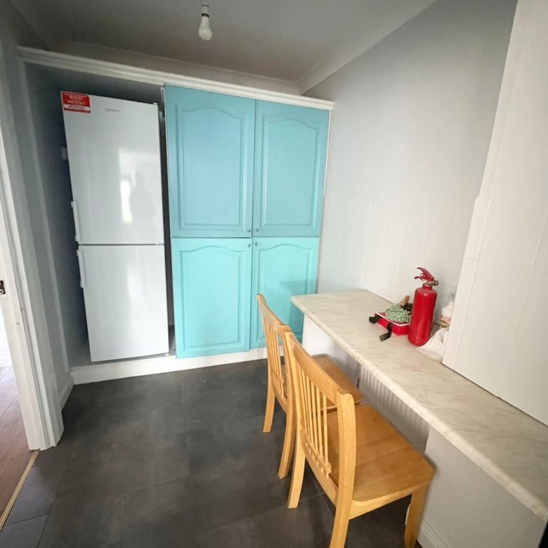 Kitchen nook with blue cabinets, white fridge, counter, and wooden chairs.