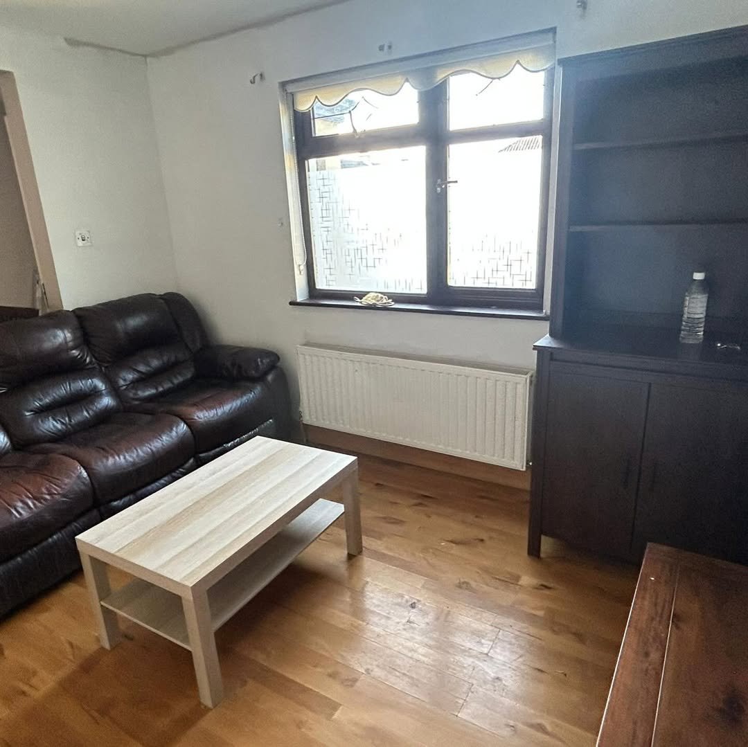 Living room with brown leather sofa, light wood coffee table, and dark wood bookcase near window.