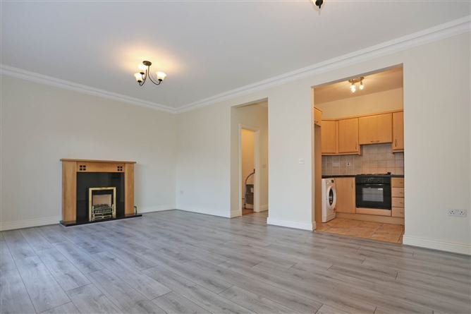 Living room with fireplace and open kitchen view, wood-look flooring.