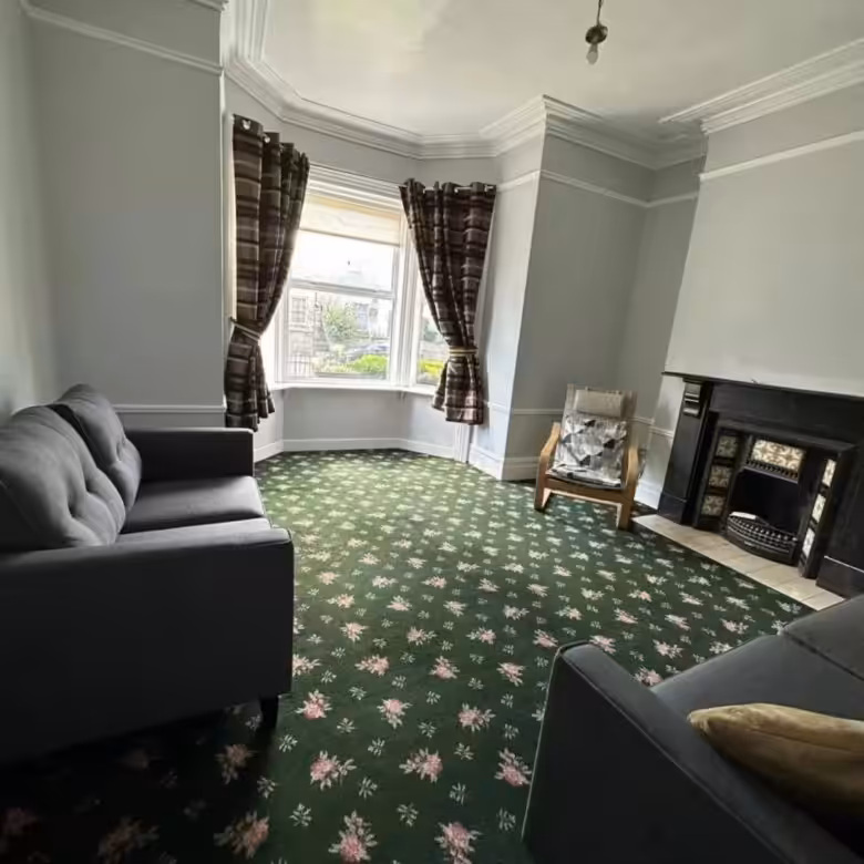Living room with green floral carpet, gray sofa, bay window, and fireplace.