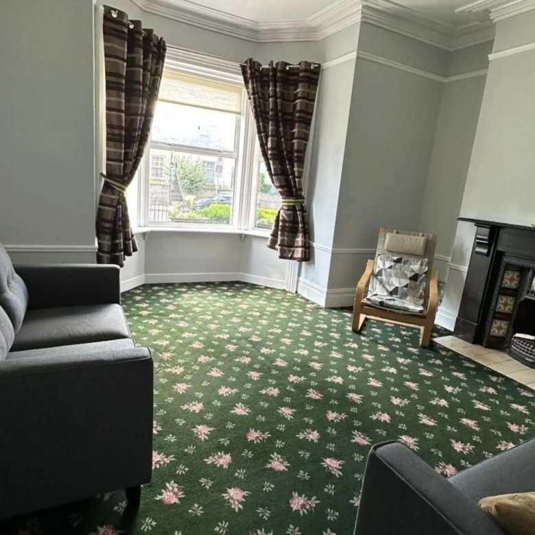 Living room with green floral carpet, gray sofa, bay window, and fireplace.