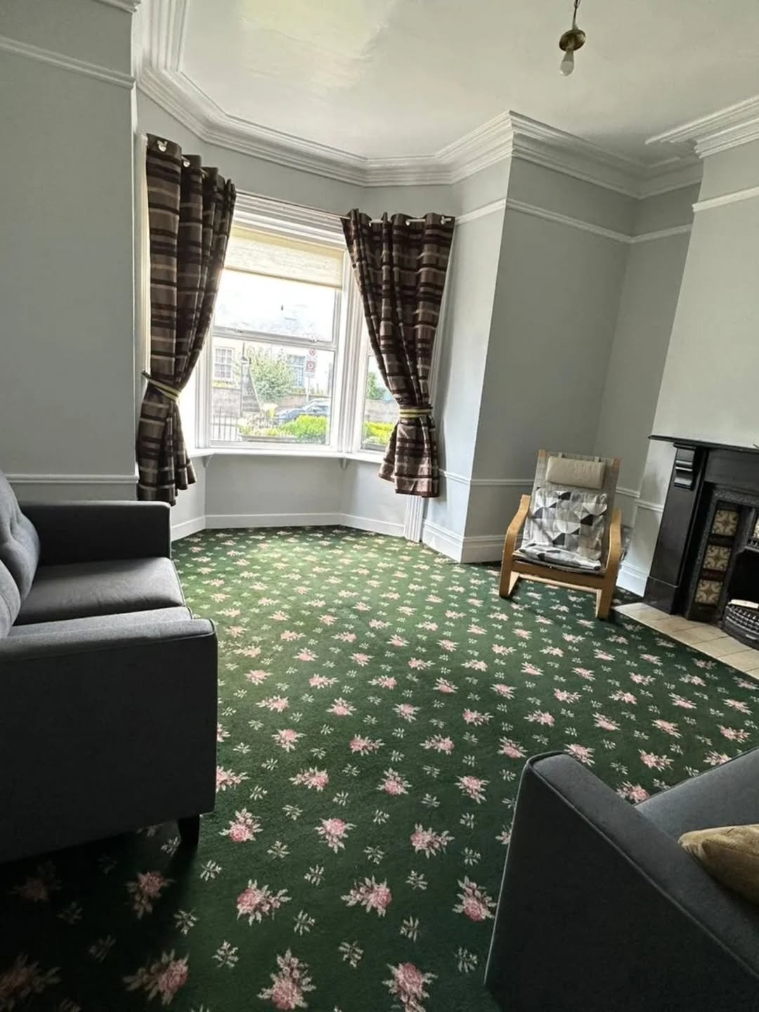 Living room with green floral carpet, gray sofa, bay window, and fireplace.