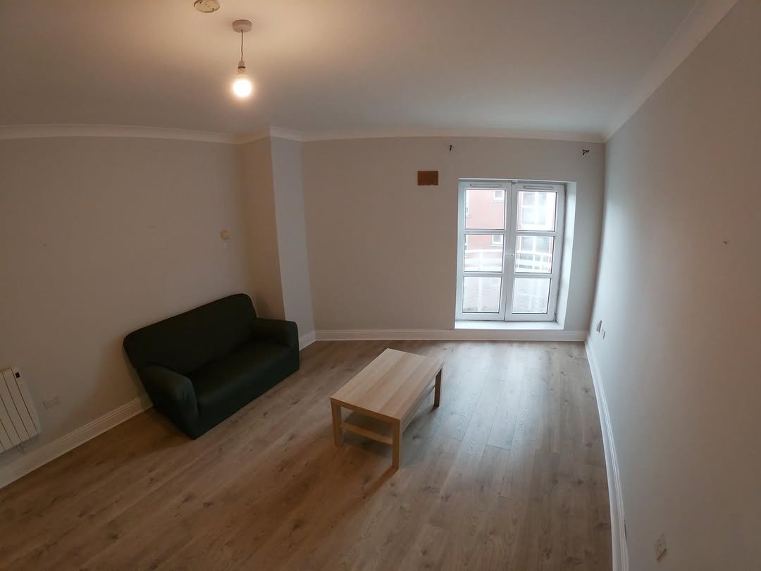 Living room with dark green sofa, light wood coffee table, and large window with natural light.