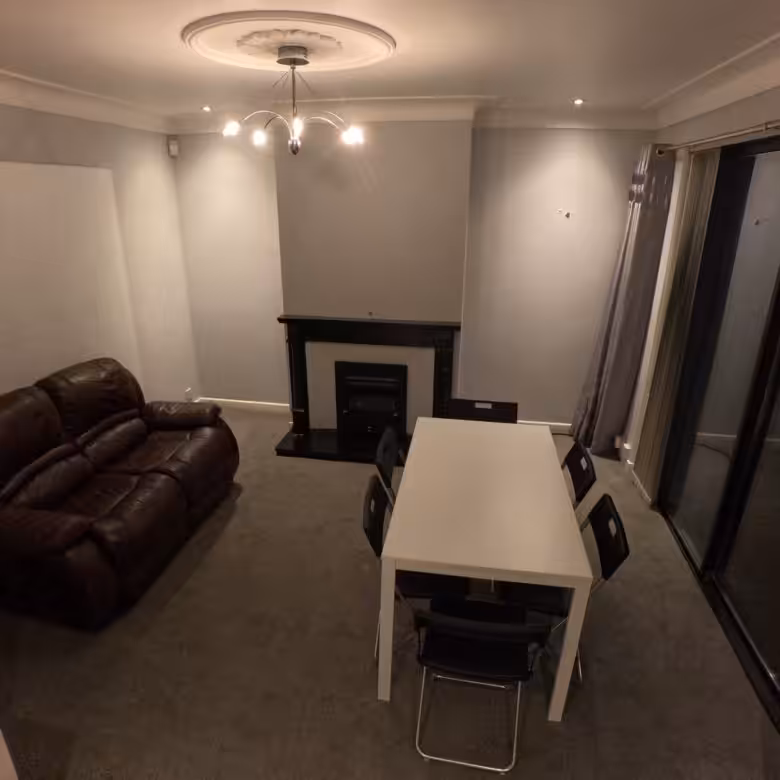 Living room with brown leather sofa, white dining table, and fireplace.