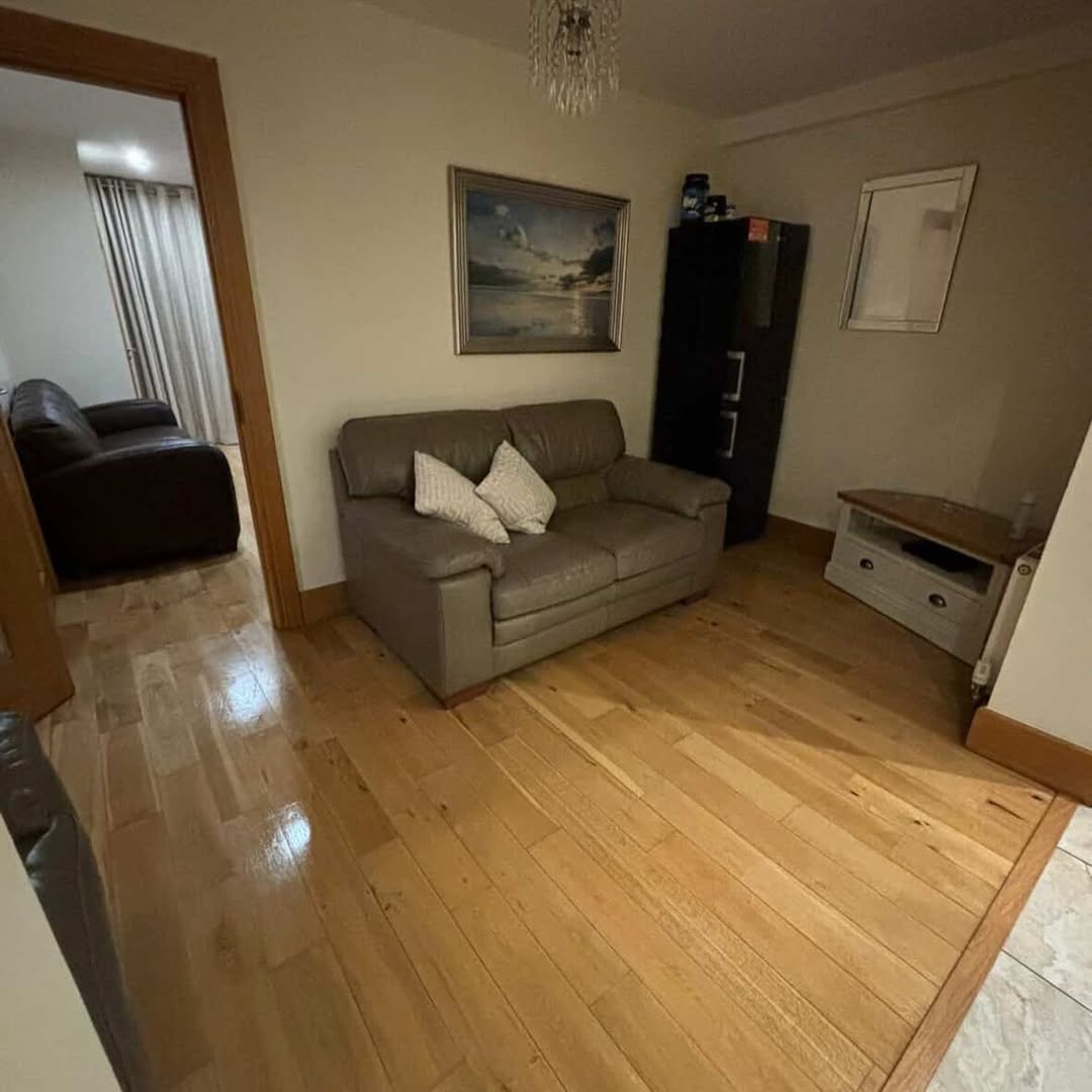 Living room with leather sofa, wood floors, and doorway to another room.