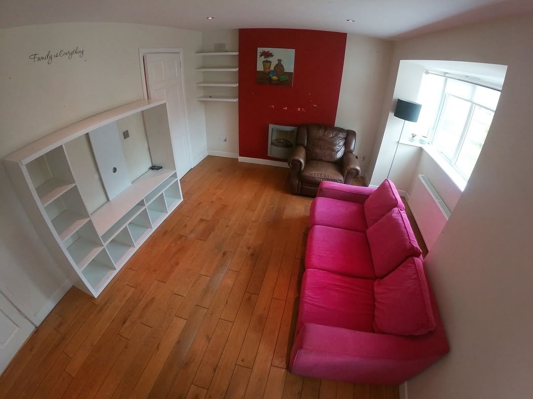Living room with pink sofa, wooden floor, and red accent wall.