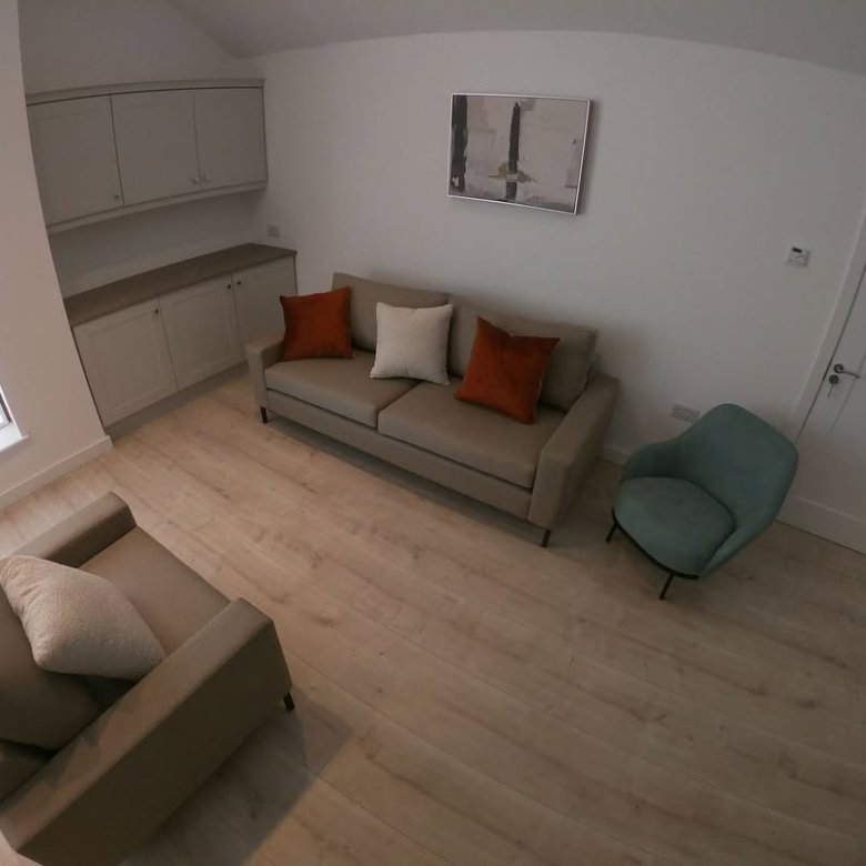 Living room with sofa, armchair, built-in cabinets, painting, door, and light wood flooring.