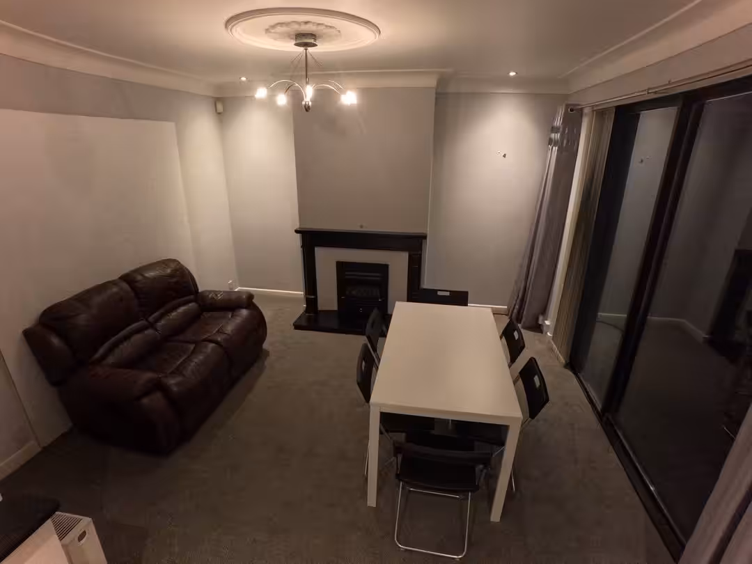 Living room with brown leather sofa, white table, black chairs, and fireplace. Gray walls and ceiling fixture.