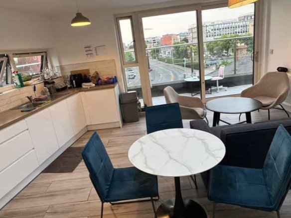 Modern apartment interior with dining area, kitchen, and balcony overlooking city. Neutral tones and blue accents.