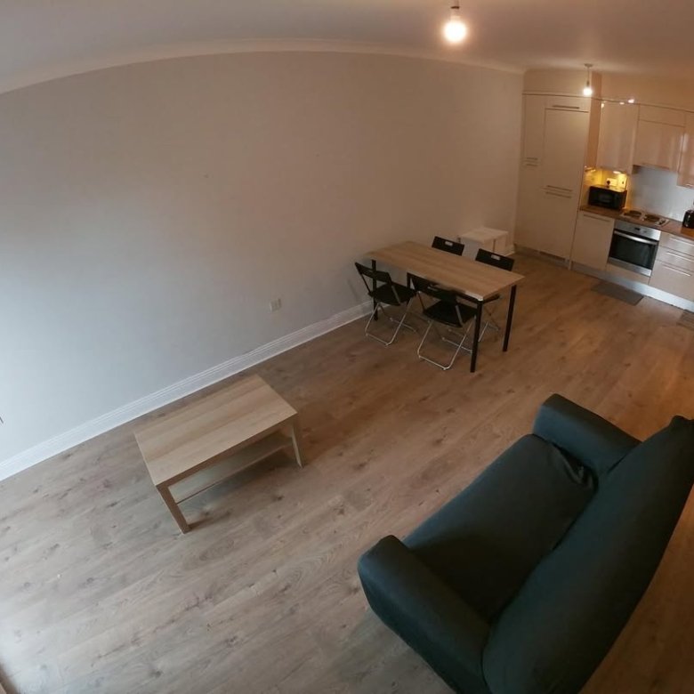 Apartment interior with sofa, table, and kitchen area. Modern design, light wood floors.