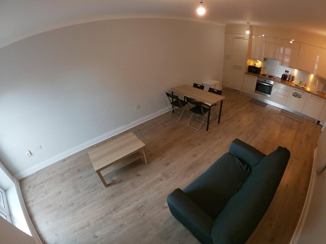 Apartment interior with sofa, table, and kitchen area. Modern design, light wood floors.