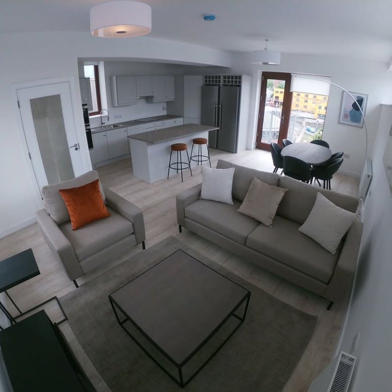 Modern apartment living room with sofa, armchair, kitchen, and dining area.