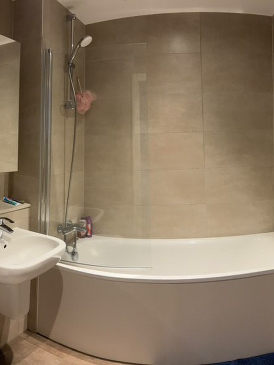 Modern bathroom with curved bathtub, glass shower screen, and beige tiles.