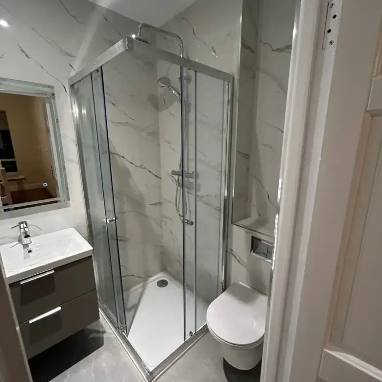 Modern bathroom with shower, toilet, sink, and marble-style tiles.