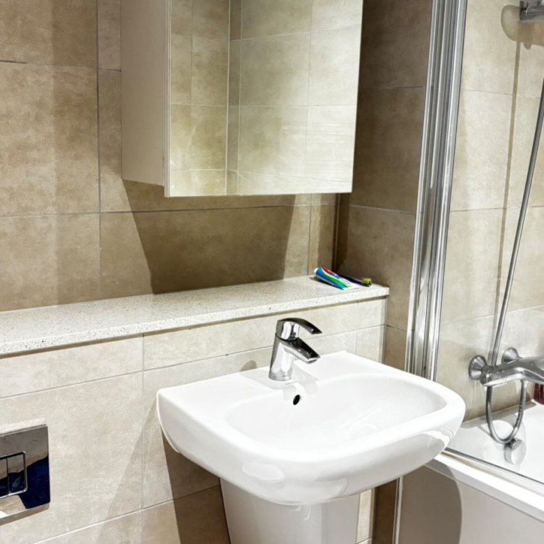 Modern bathroom: white sink, mirrored cabinet, beige tiles, and shower screen.