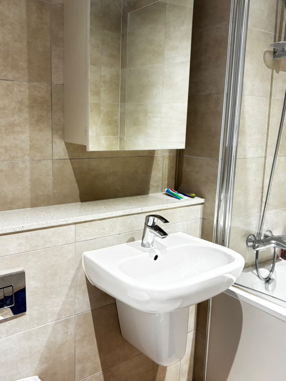 Modern bathroom: white sink, mirrored cabinet, beige tiles, and shower screen.