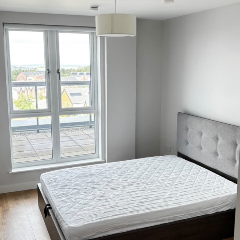 Modern bedroom with bed, headboard, large window, and wood floor. Neutral color scheme.