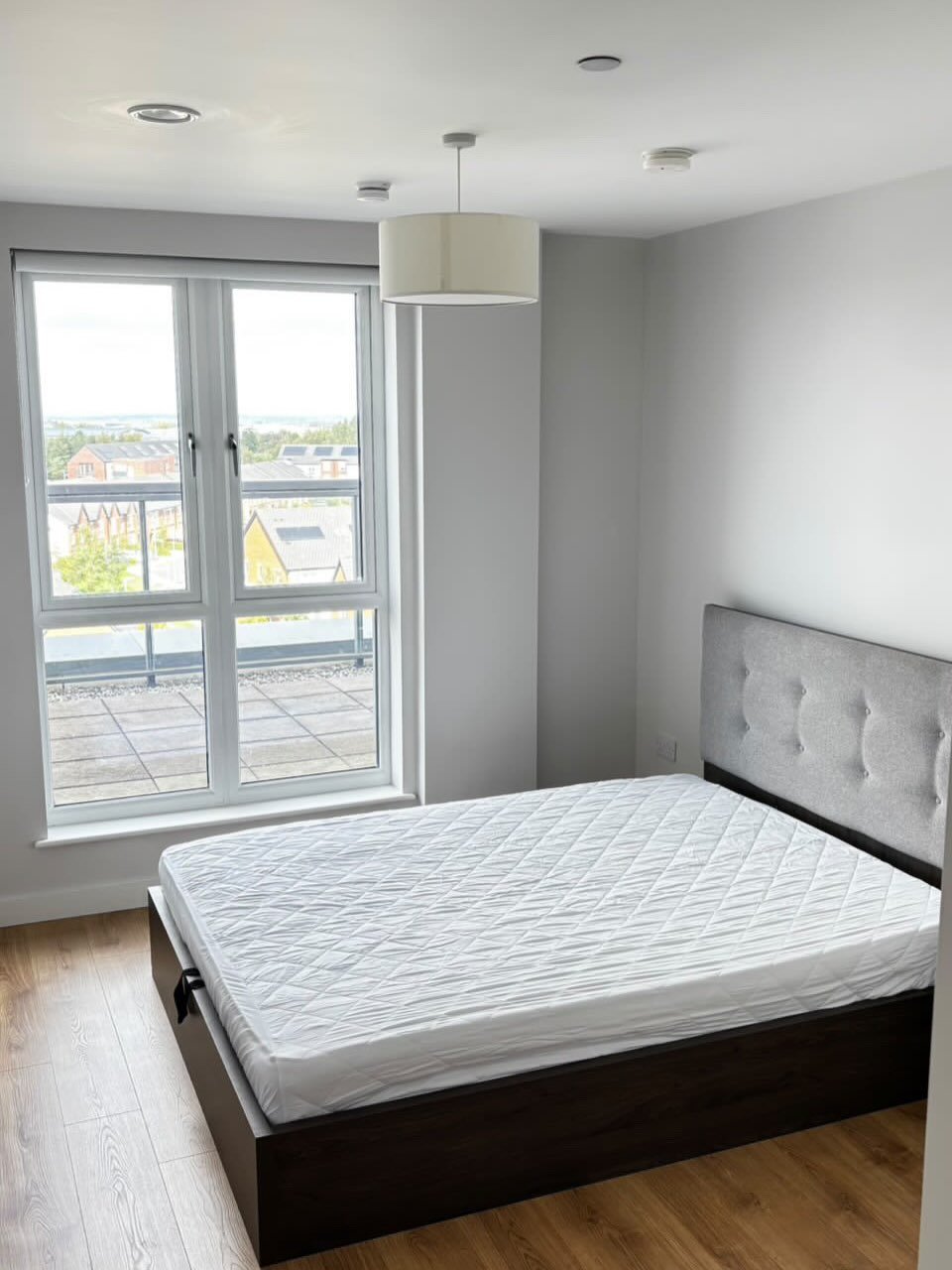 Modern bedroom with bed, headboard, large window, and wood floor. Neutral color scheme.