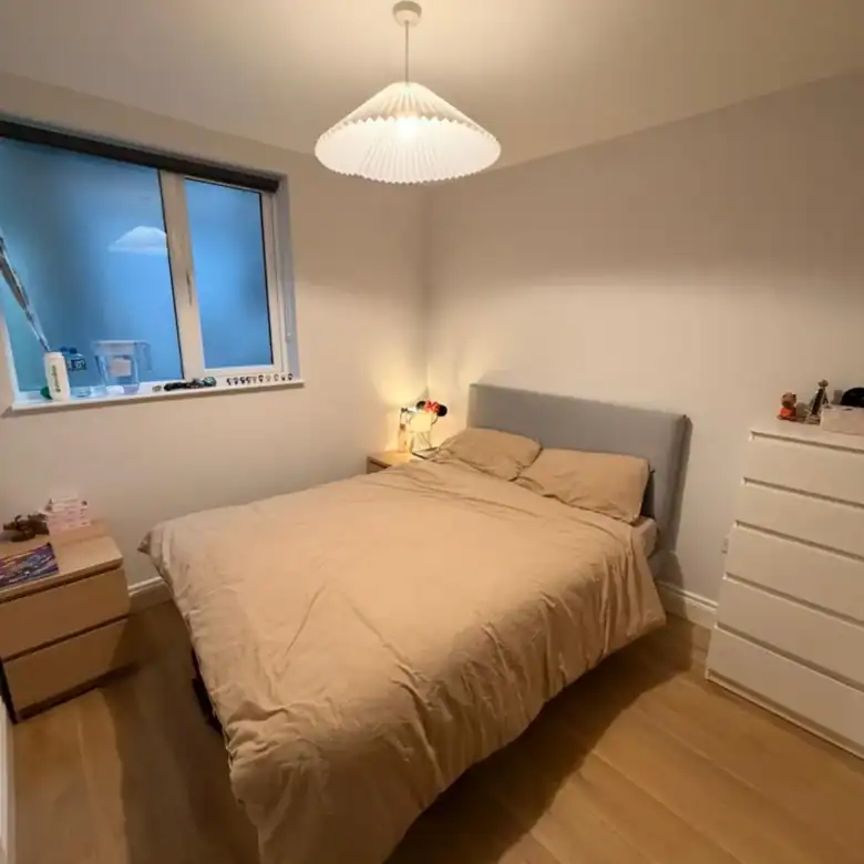 Cozy bedroom with double bed, nightstand, and white dresser. Modern, minimalist design.