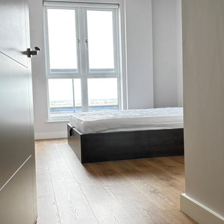 Bedroom with modern bed, wood floors, and bright window.