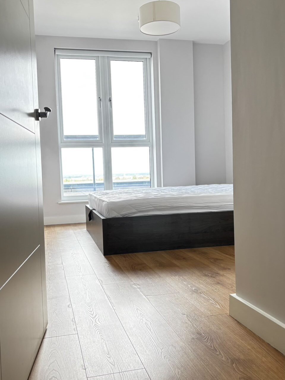 Bedroom with modern bed, wood floors, and bright window.
